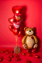 A large foil bear and a set of balloons in the form of hearts for Valentine's Day on a red background. Inscriptions in Russian balloons: "You are a miracle", "My love".