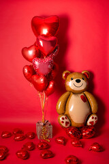 A large foil bear and a set of balloons in the form of hearts for Valentine's Day on a red background.