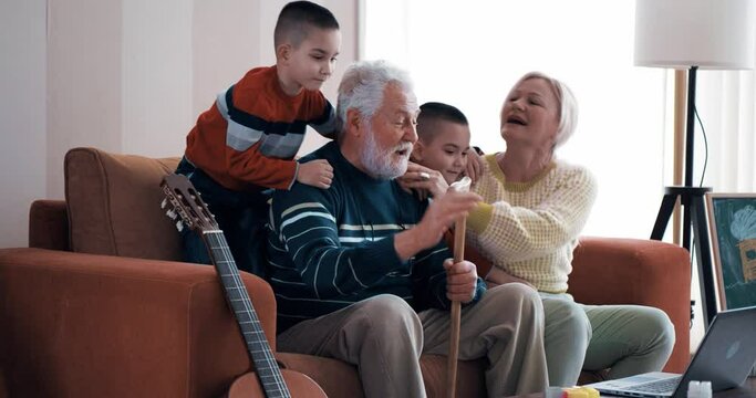 The gray-haired grandfather with the stick talked on a video call with the family. A multi-generational family sits on a sofa and talks to the family using a laptop
