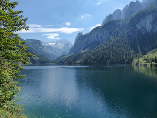 Panoramic view on Gosau lake, with Dachstein glacier in the back in Austrian Alps. The lake is surrounded by high mountains, overgrown with tall trees. Sun reflects on the surface. Serenity  and calm