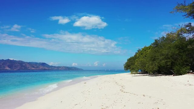 A Soothing Scenery Of A Tropical Environment Featuring A White Sand Beach With Luscious Plants And Tall Trees Nearby The Wide Waving Turquoise Sea, Slowly Zooming In.