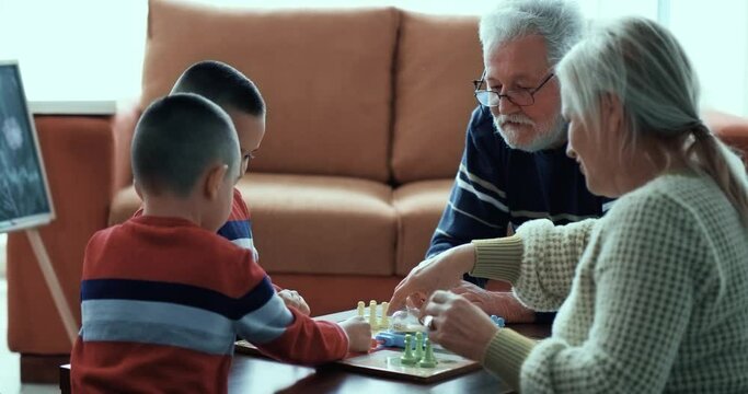 Old grandfather and  grandmother are playing board games with the twins grandchild