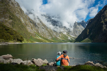 A Couple sitting on the shore of Lake Marian, enjoying the views, Fiordland National Park, New Zealand