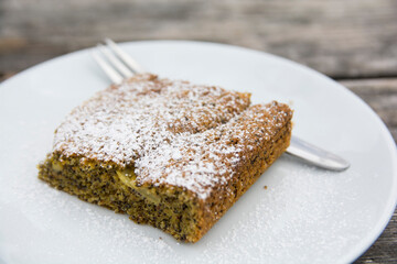 A slice of Poppy seed cake, served in a plate, covered with sugar powder