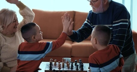 Bearded grandfather gives hi-five to his little grandchildren and grandmother after the chess game is over. - Powered by Adobe