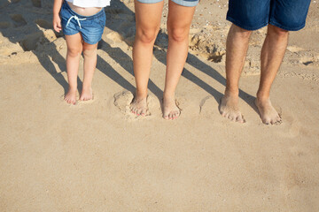 Legs and feet of three family mother father and child standing on sand sea beach