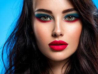 Portrait of beautiful young woman with bright blue makeup. Beautiful brunette with bright red lipstick on her lips. Pretty girl with long black hair. Closeup face of brunette woman. Sexy girl.