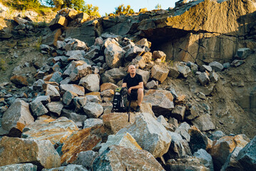 Handsome man with backpack in the mountains in summer time. Male tourist surrounded by high and big rocks. Closeup.