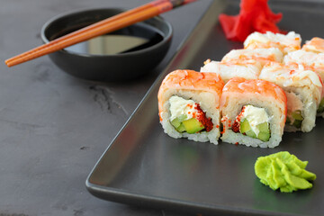 Sushi roll covered with shrimp meat on black ceramic plate