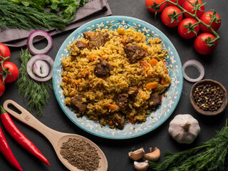 A large plate filled with pilaf, next to cherry tomatoes, fresh pepper . garlic, zeros and a mixture of peppers. All on a dark background.