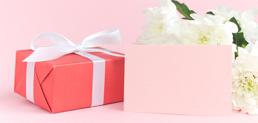 Red present gift box and white chrysanthemums with space for greeting text on pink background. Card for Valentines, Mom, Women's day and 8 March. Copy space, mock up, banner.