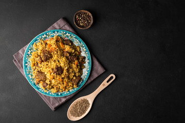 Fragrant pilaf with meat and vegetables top view on a plate on black background with copy space.
