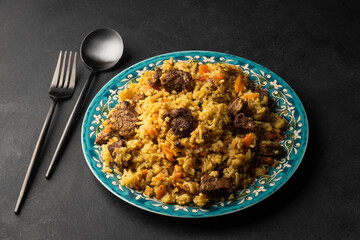 Fragrant pilaf with meat and vegetables top view on a plate on black background with copy space.