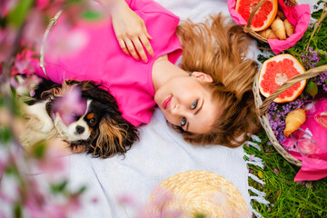 Top view young women on a picnic, lying on a blanket. A woman holds a dog. Next to the basket....