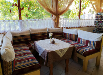 The interior of an empty Crimean Tatar cafe in Bakhchisarai. Sofas, table and view from the window to green trees in summer. Travel concept.