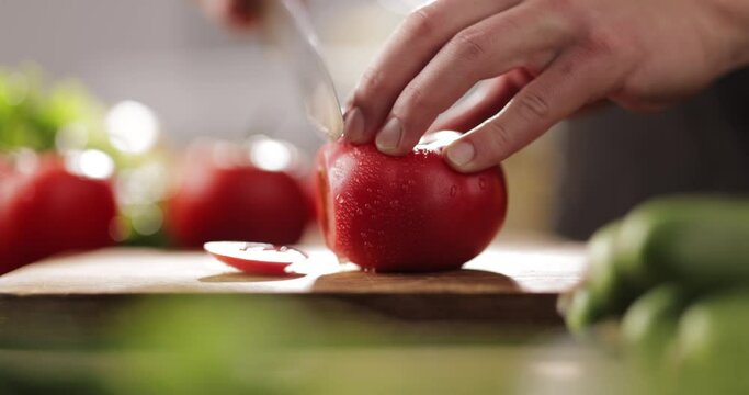 Chef cutting fresh tomato with knife on wooden board. Chef preparing vegetarian meal in the kitchen, 4k footage