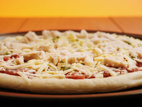 Traditional pizza with chicken meat on a round metal trey. Selective focus. Uncooked product. Ready meal industry.