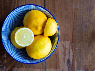 Top view of lemons in a bowl on wooden table with space