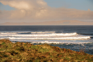 View on Atlantic ocean. Mullaghmore peninsula county Sligo. Powerful waves rolling in the ocean. Cloudy sky. Rough stone coast line. Warm sunny day