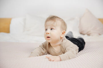 Surprised little baby man lies on bed and looks to side, place for text