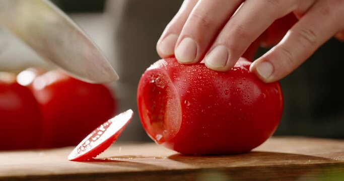 Chef cutting fresh tomato with knife on wooden board. Chef preparing vegetarian meal in the kitchen, 4k footage