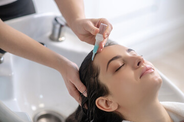 Hair stylist applying keratin on young womans hair