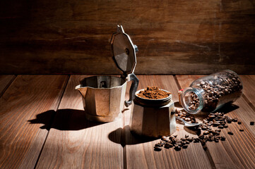 A geyser type metal coffee maker, photographed against a vintage wooden background with coffee beans.