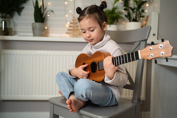 Little girl plays ukulele. Creative development in children. Musical education from childhood. Teaching music online at home