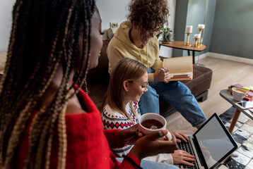 Multiethnic female students learning at home using laptop and books for research.	