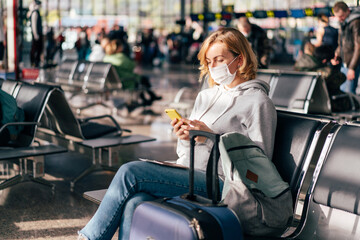 A European woman in a protective medical mask on her face sits at the airport waiting for a flight...