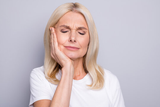Photo of pensioner lady palm cheekbone suffer toothache closed eyes wear white t-shirt isolated grey color background