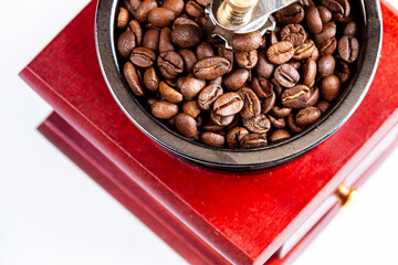 close-up of a dark red coffee grinder and coffee beans on white background