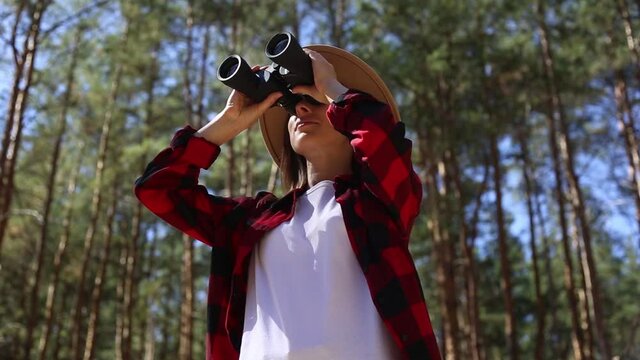 Girl in a hat looks through binoculars in the forest. Concept hike, tourism.