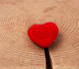 red velvet heart on a wooden background lies on a crack in the tree. relationship concept, risk of breaking up.