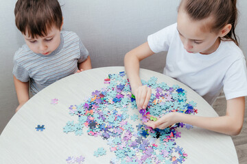 Happy boy and a girl collect a puzzle sitting at a table
