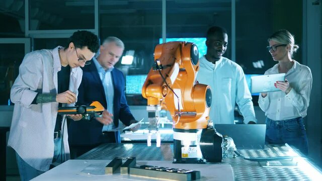 Team of researchers are holding an experiment with a robotic arm. Professional engineers working at modern industrial laboratory.