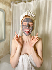 beautiful woman applied a gray clay mask to her face in the bathroom. Beauty treatments at home.