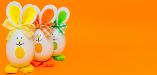 Three Easter eggs with bunny ears on spring yellow background.