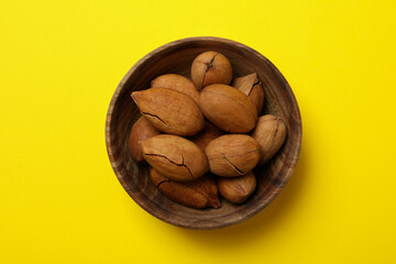 Bowl with tasty pecan nuts on yellow background