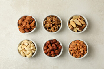 Bowls with different nuts on white textured background, top view