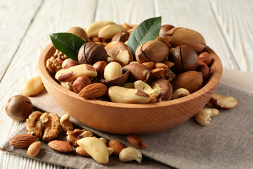 Bowl with different tasty nuts on white wooden background