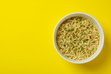 Cooked instant noodles in paper cup on yellow background