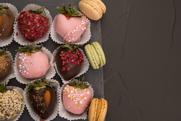 Assorted strawberries in chocolate with macaron, sweet dessert, free space for your text, sprinkled with nuts, top view, dark background.