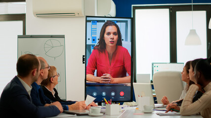 Obraz premium Diverse executive team meeting at conference video call looking at huge display. Business people talking to webcam, do online conference participate internet brainstorming, distance office discussion