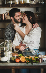 Fototapeta na wymiar Sweet young family couple cookin together in the kitchen. Young caucasian man and brunette woman with faces stained in flour hugging, laughing and making dough for baking citrus cake. Valentines Day
