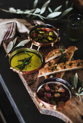 Pickled Greek olives, olive oil and herbed focaccia slices on rustic wooden board, selective focus. Traditional Mediterranean meze appetizers platter