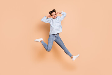 Fototapeta na wymiar Full size profile photo of optimistic nice brunette lady jump show v-sign wear blue sweater jeans sneakers isolated on beige background