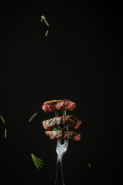 Grilled beef steak on a fork adding rosemary in a freeze motion on black background. vertical image, place for text.