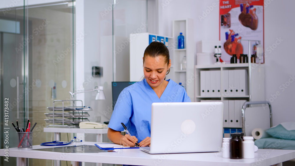 Wall mural Nurse taking notes on clipboard after reading medical raports of patient from laptop. Healthcare physician in uniform, doctor assistant working in hospital checking registration, writing treatments