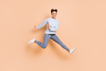 Fototapeta na wymiar Full size profile photo of optimistic nice brunette lady jump run wear blue sweater jeans sneakers isolated on beige color background
